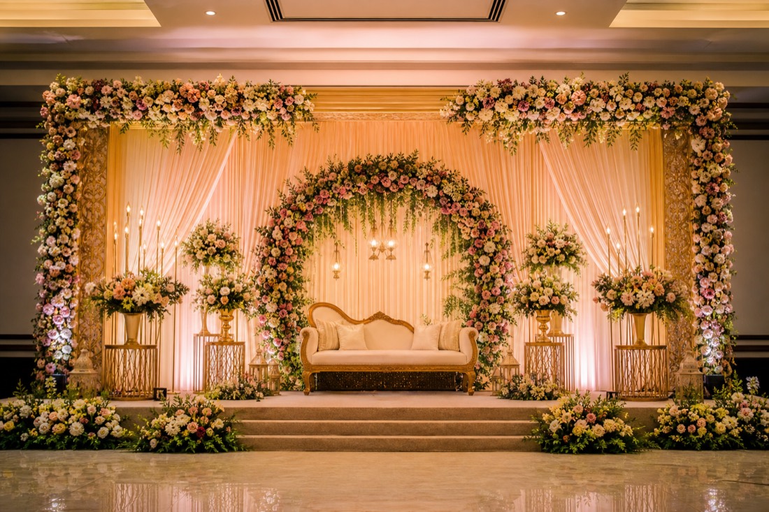 Wedding reception stage in Hyderabad with a pastel floral arch, draped backdrop and a gold couple couch