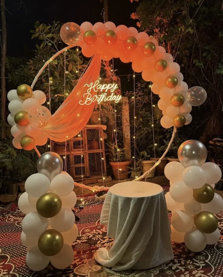 Outdoor birthday decoration in Hyderabad with a gold and white balloon ring arch, neon Happy Birthday sign and fairy lights